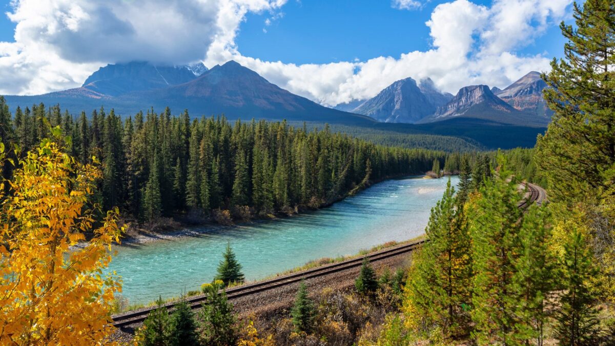 Spoorlijn langs een turquoise rivier met op de achtergrond de bergtoppen van Banff National Park in Canada – reizen met Explore