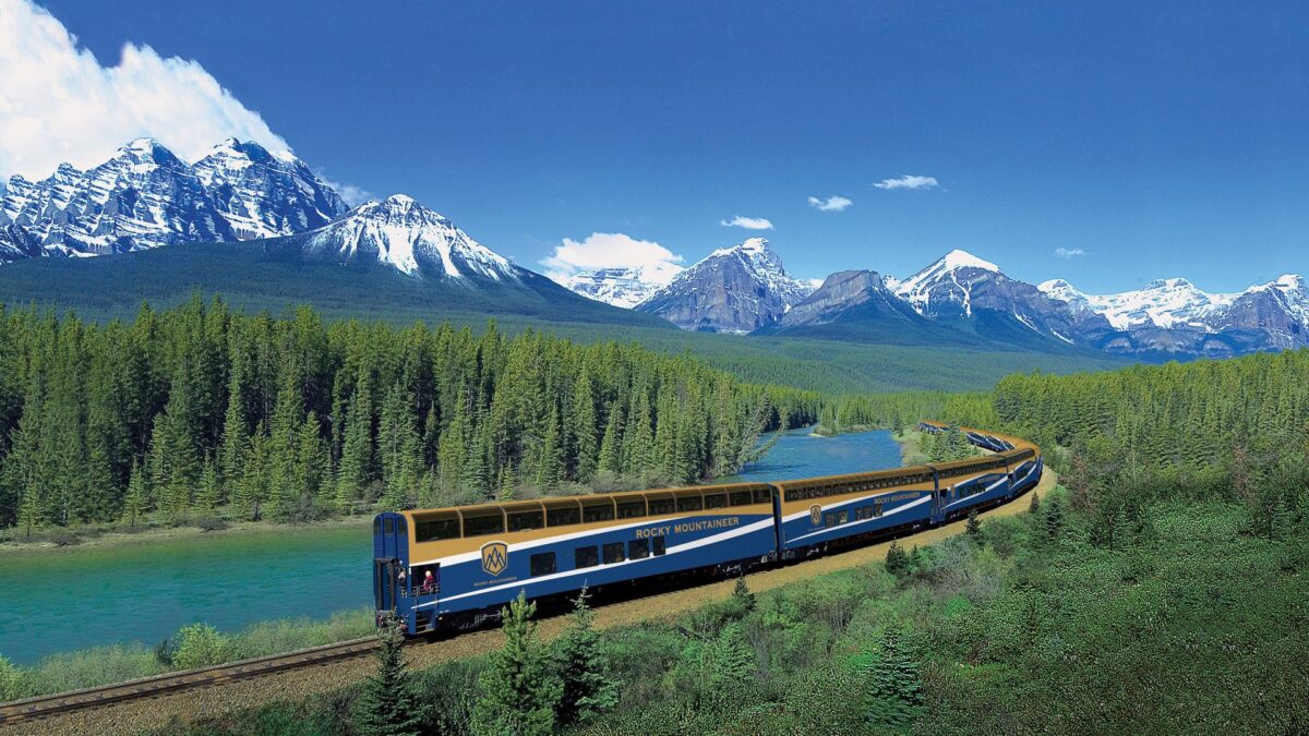 De Rocky Mountaineer rijdt door een weids berglandschap met besneeuwde toppen en groene naaldbossen langs een turquoise rivier – Canada – reizen met Explore