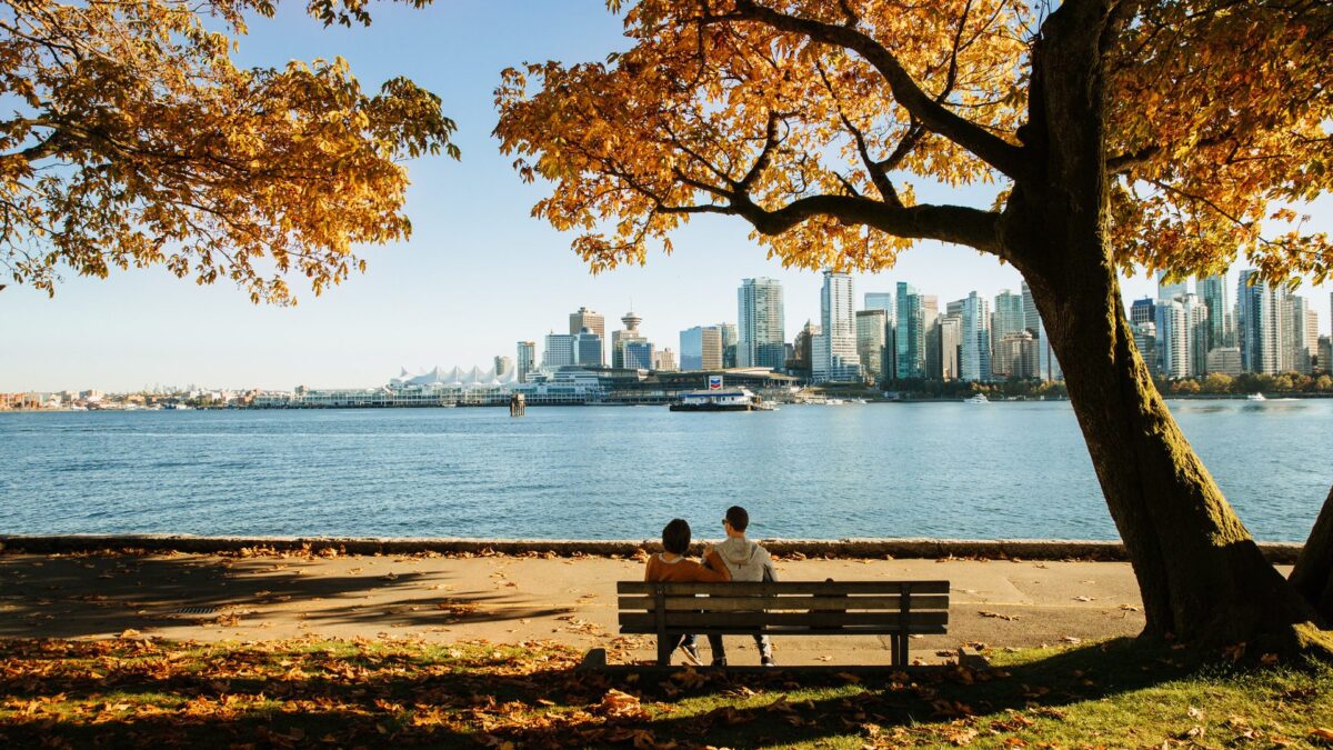 Koppel zit op een bankje onder herfstbladeren met uitzicht op de skyline van Vancouver in Canada – reizen met Explore