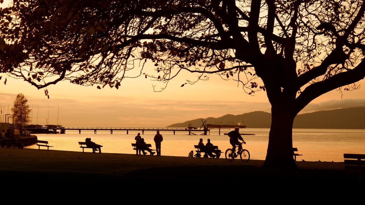 Mensen ontspannen in Stanley Park in Vancouver, Canada, tijdens een zonsondergang met uitzicht op zee en bergen – reizen met Explore