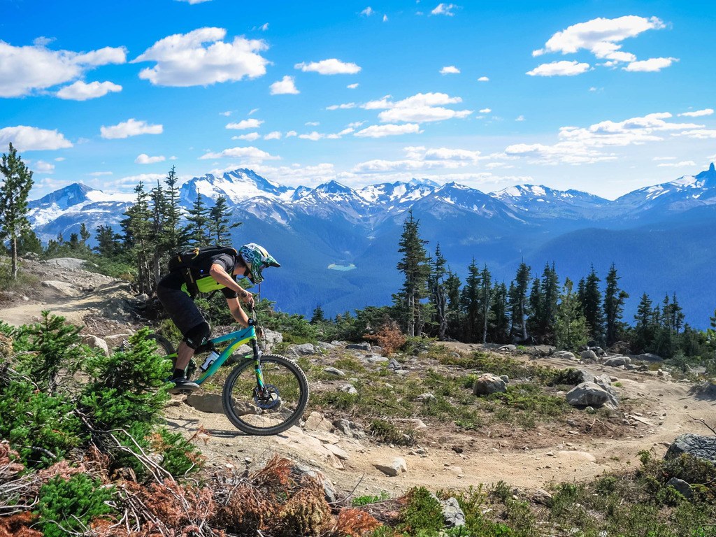 Mountainbiker op een ruig pad in Whistler, Canada, omringd door met sneeuw bedekte bergen – reizen met Explore
