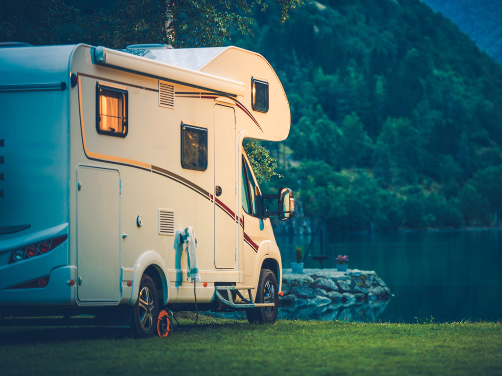 Camper geparkeerd aan het water bij schemering, omgeven door groen en bergen, Canada – reizen met Explore.