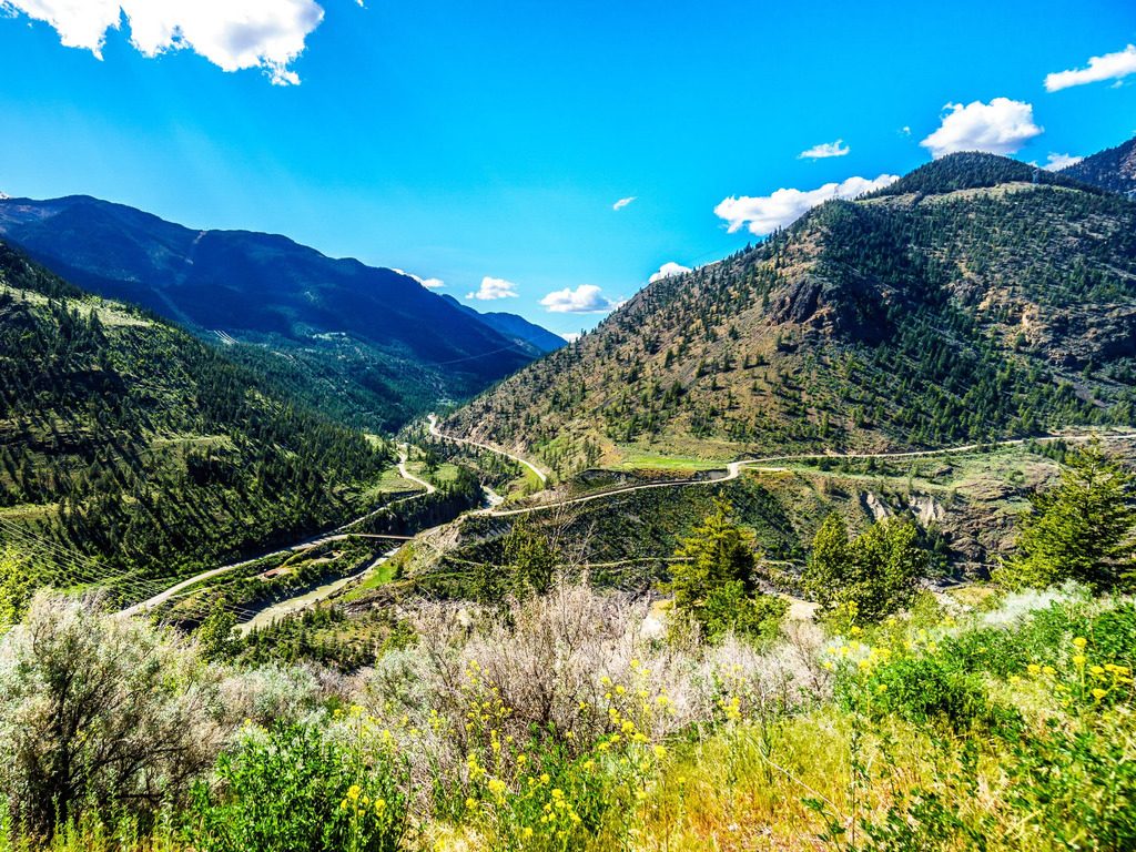 Kronkelende weg door de Bridge River Valley, omringd door groene bergen en wilde bloemen – Canada – reizen met Explore.