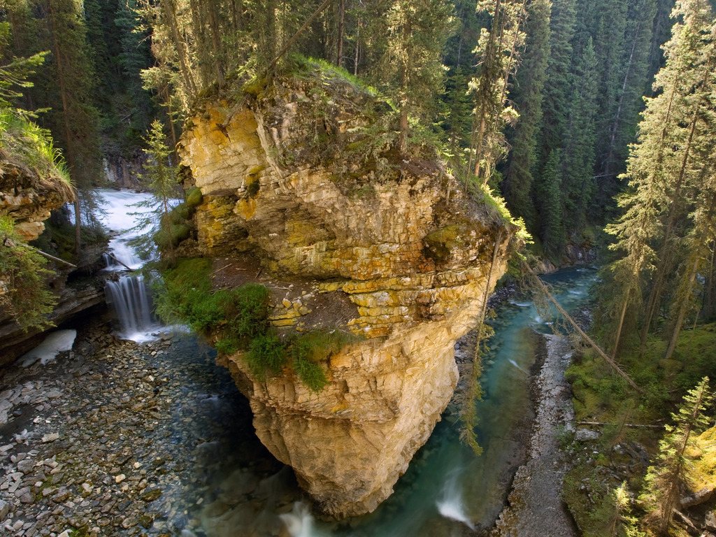 Rotsformatie met waterval en stromende rivier omgeven door dicht bos in Banff National Park, Alberta, Canada – reizen met Explore.