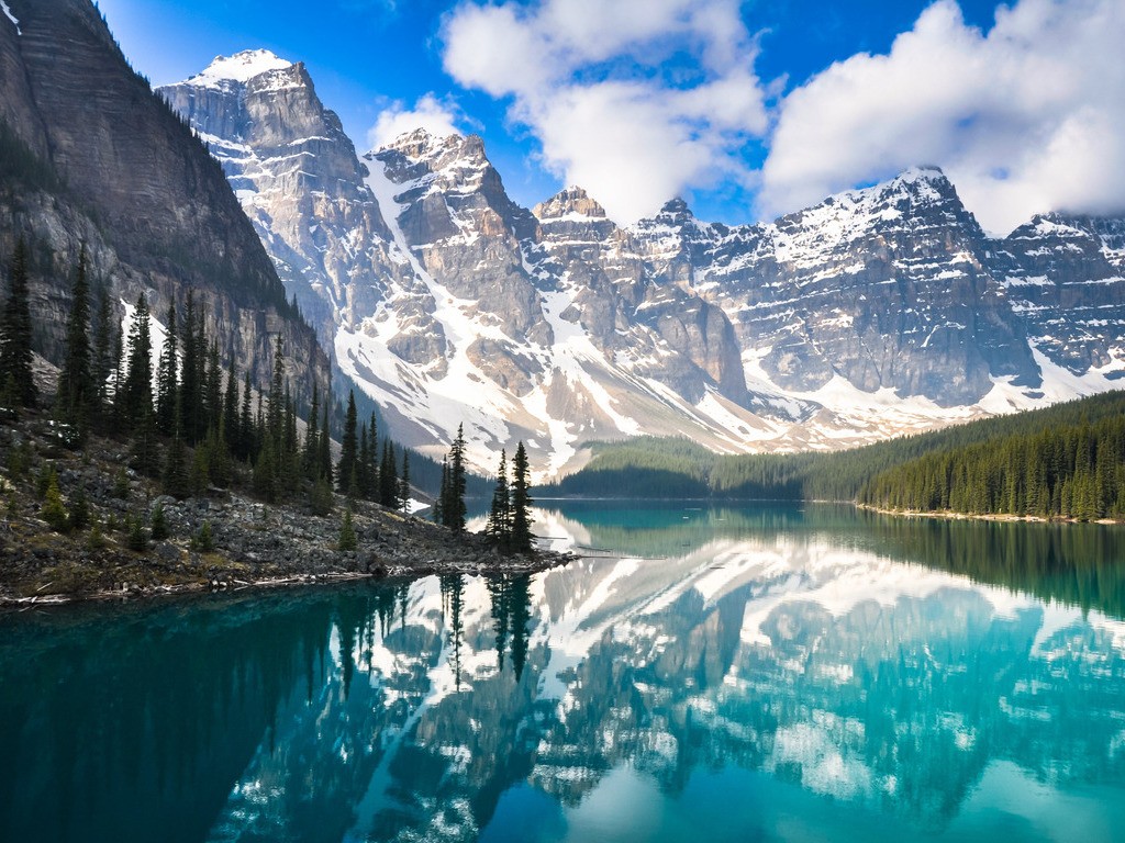 Besneeuwde bergtoppen weerspiegeld in het heldere turquoise water van Moraine Lake, Canada – reizen met Explore.