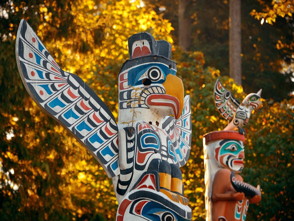 Totempalen in Stanley Park, kleurrijk beschilderd en omringd door herfstbladeren – Canada – reizen met Explore.