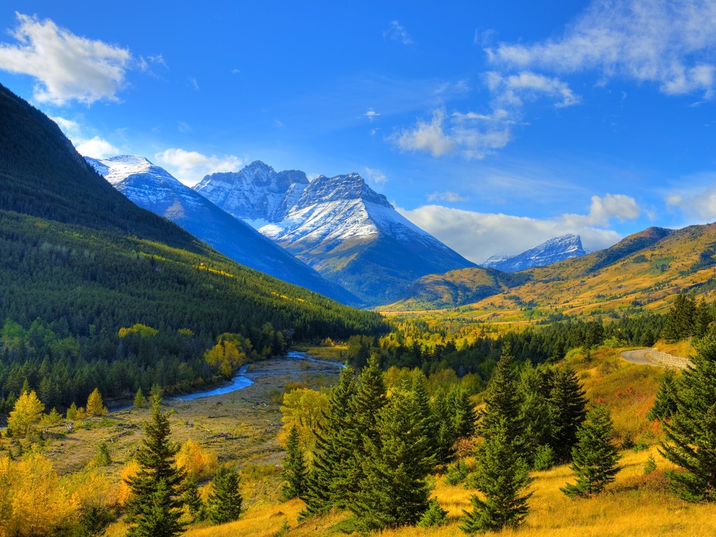 Vallei met dennen en herfstkleuren, besneeuwde bergen en blauwe lucht in Waterton National Park, Canada – reizen met Explore.