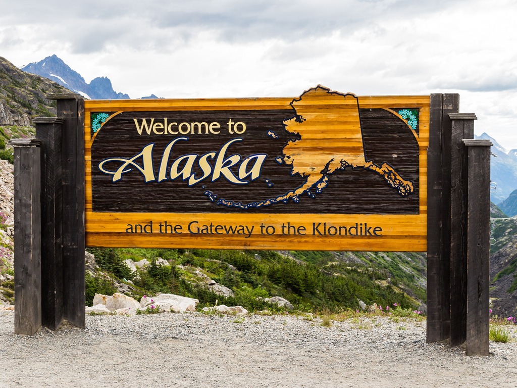 Welkomstbord aan de grens tussen Yukon en Alaska, omringd door bergen – reizen met Explore.