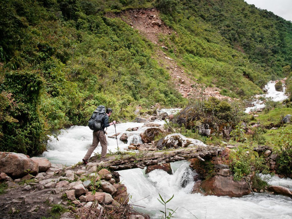 Wandelaar steekt riviertje over tijdens Salkantay-trek in Peru – reizen met Explore.