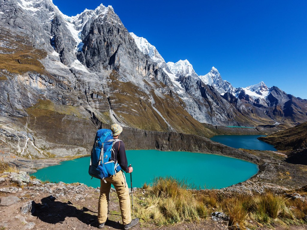 Wandelaar met rugzak kijkt uit over turquoise meren en besneeuwde bergen in de Andes, Peru – reizen met Explore.