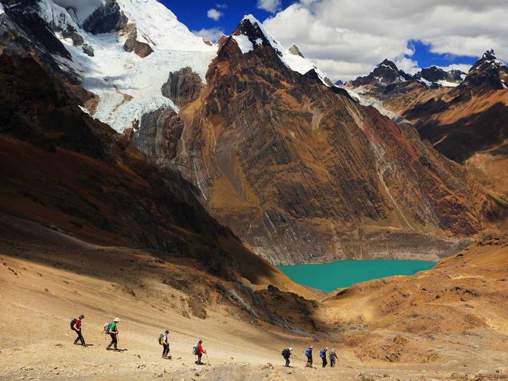 Wandelaars dalen af langs een bergpad met uitzicht op een turquoise meer in de Andes, Peru – reizen met Explore.