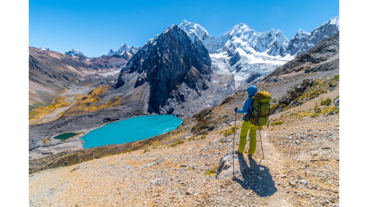 Wandelaar kijkt uit over een helder turquoise bergmeer en besneeuwde toppen in de Andes, Peru – reizen met Explore.